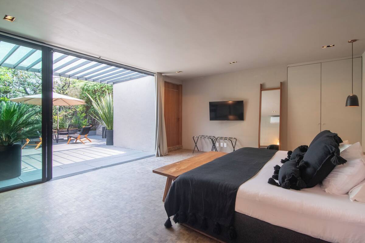 A modern bedroom with a large bed, a TV, and a sliding glass door leading to an outdoor patio.