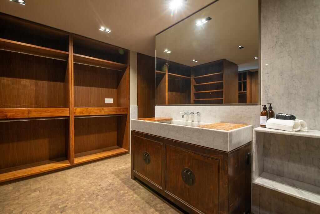 A modern bathroom with a wooden vanity, a large mirror, and built-in shelving.