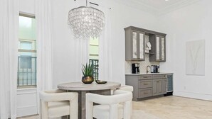 Zona pranzo con tavolo rotondo, due sedie, un lampadario e cucina con pensili e piano di lavoro.