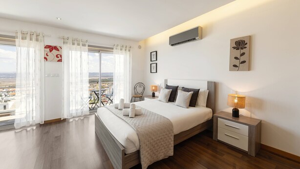 A modern bedroom with a large bed, bedside tables, and a view of the city.