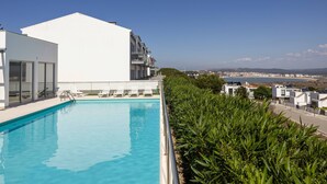 A rooftop pool with white lounge chairs and a view of the city.