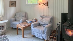 Een gezellige woonkamer met gestreept meubilair, een houten bijzettafeltje met een puzzel, een open haard en een raam met uitzicht op groen.