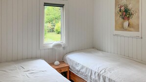 Een kamer met twee eenpersoonsbedden, een raam met uitzicht op groen, een witte lamp op een houten nachtkastje, en een schilderij aan de muur.