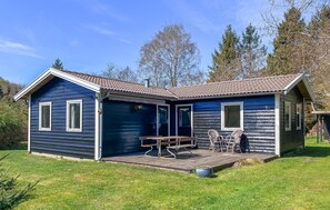 Une petite cabane en bois d’un seul étage, avec un toit recouvert de tuiles, une terrasse couverte avec une table et des chaises, et le chiffre « 3 » peint sur le côté.