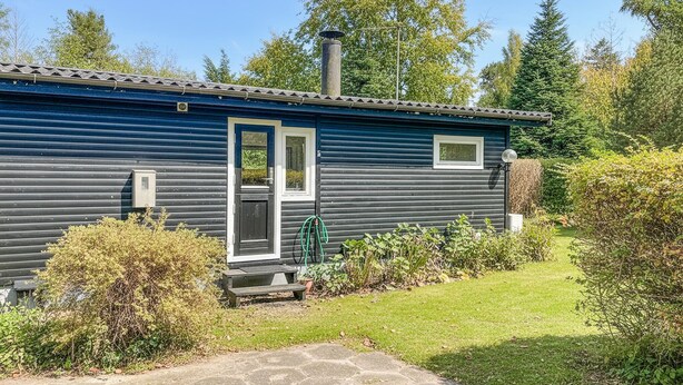 Een gelijkvloers vakantiehuisje met een donkerblauwe buitenkant, een voordeur en een klein terras.