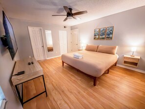 A bedroom with a bed, bedside table, lamp, ceiling fan, and a wall-mounted TV. - Charming Home Minutes from Parks (Kissimmee)