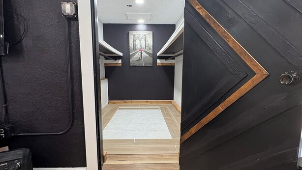 Un couloir doté d’un plancher en bois, une porte noire ornée d’un motif géométrique et un tableau représentant un pont accroché au mur.