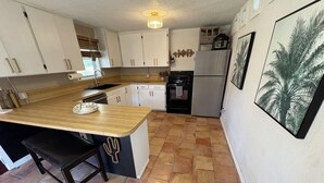 Une cuisine avec des meubles blancs, un plan de travail en bois, une cuisinière noire et un réfrigérateur.