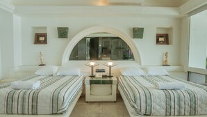Quarto de hotel com duas camas, piso de mármore, uma grande janela em arco e quadros nas paredes.