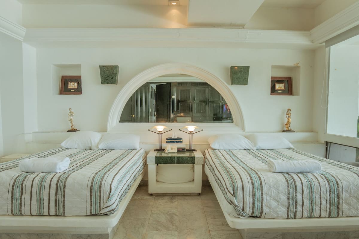 Een hotelkamer met twee bedden, een marmeren vloer, een groot boogvenster en ingelijste foto's aan de muur.