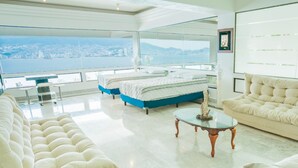 Uma sala de estar espaçosa com uma grande janela dando para a paisagem urbana. Há um sofá, uma mesa de centro e uma cama com vista.