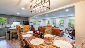 Un comedor amplio con una mesa de madera, sillas tejidas y una lámpara colgante moderna.