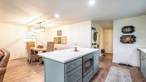 Amplia sala de estar con una isla grande, mesa de comedor y sillas. Hay un cuarto de lavado con lavadora y secadora.