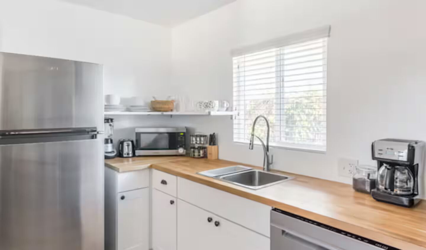 Una cocina moderna con electrodomésticos de acero inoxidable, encimera de madera y ventana con persianas.