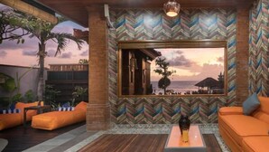 Un salon moderne avec des canapés orange, une table basse en bois et une grande fenêtre donnant sur la plage et l’océan.