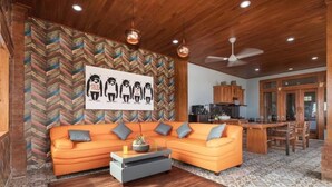 Un salon moderne avec un mur orné d’un motif en chevron, un canapé d’angle, une table basse et un coin cuisine à l’arrière-plan.