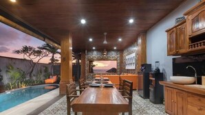 Un espace repas avec une piscine, des meubles en bois et une vue sur le coucher du soleil.