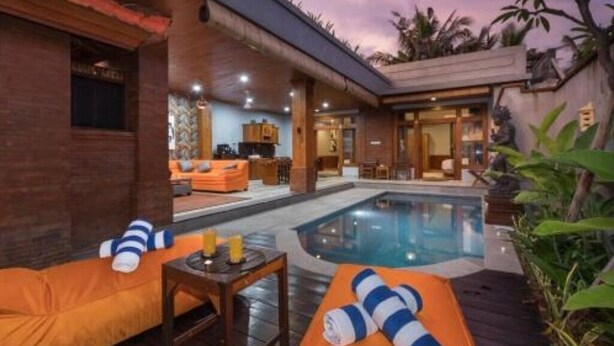 Un espace aménagé au bord de la piscine, avec un fauteuil de relaxation et une table, une petite piscine et une vue sur l’intérieur du bâtiment.