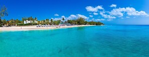Ein Strand mit klarem türkisblauem Wasser, einem Sandstrand und einer Reihe von Strandsonnenschirmen.