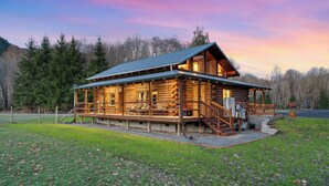 A log cabin with a porch, a staircase, and a view of the surrounding forest. - Spacious Cabin on 65 acres with no neighbors (Randle)