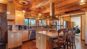 A modern kitchen with wooden cabinets, stainless steel appliances, and a large island with bar stools. - Spacious Cabin on 65 acres with no neighbors (Randle)