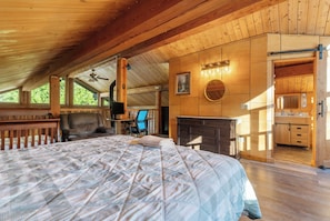 A spacious bedroom with a large bed, a desk, and a chair, a fireplace, and a bathroom with wooden cabinets. - Spacious Cabin on 65 acres with no neighbors (Randle)