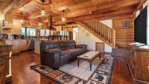 A cozy cabin interior with a wooden staircase, a leather sofa, and a kitchen area. - Spacious Cabin on 65 acres with no neighbors (Randle)