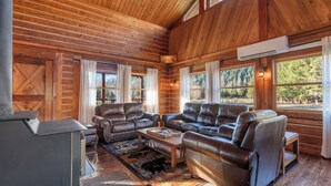A log cabin interior with a leather sofa set, a fireplace, and large windows offering a view of the forest. - Spacious Cabin on 65 acres with no neighbors (Randle)