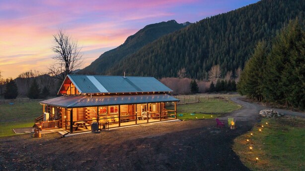 A log cabin with a metal roof, surrounded by a forest and a mountain in the background. - Spacious Cabin on 65 acres with no neighbors (Randle)