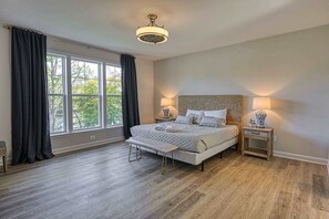 Un dormitorio con una ventana grande, una cama, mesitas de noche y un banco.