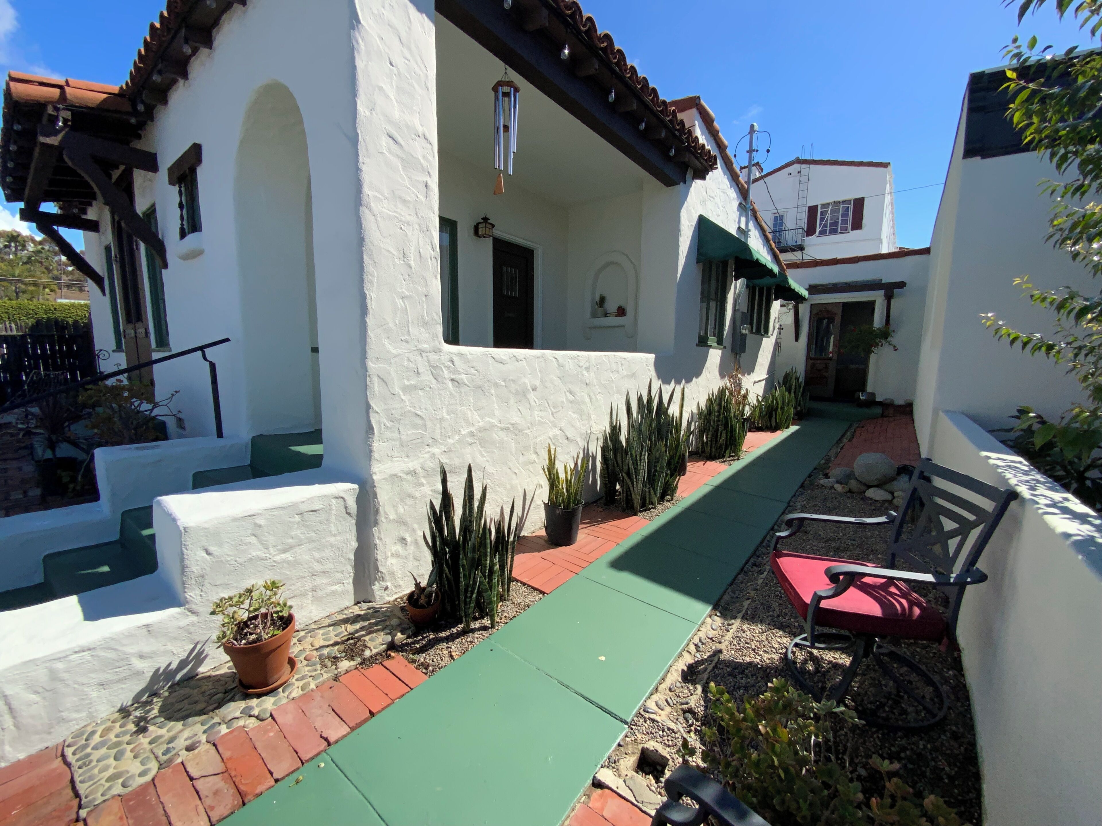 A white building with a green roof, a paved walkway, and potted plants.