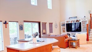A spacious living area with a large wooden island, bar stools, a television, and a staircase leading to an upper level. - Lakefront Retreat - Mile Marker 42 - Dock Bar + Sleeps 15! (Roach)