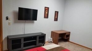 A room with a TV mounted on the wall, a wooden desk, and a grey entertainment unit.