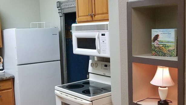 A compact kitchen with a stove, microwave, and refrigerator. A clock is mounted on the wall above the stove.