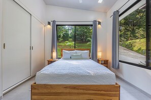 A bedroom with a large bed, a view of a garden through a window, and a sliding door on one side. - 3-bedroom 2 bath Modern Jungle Home w/ Pool and AC, 5 minutes to Beach or Uvita (Uvita)