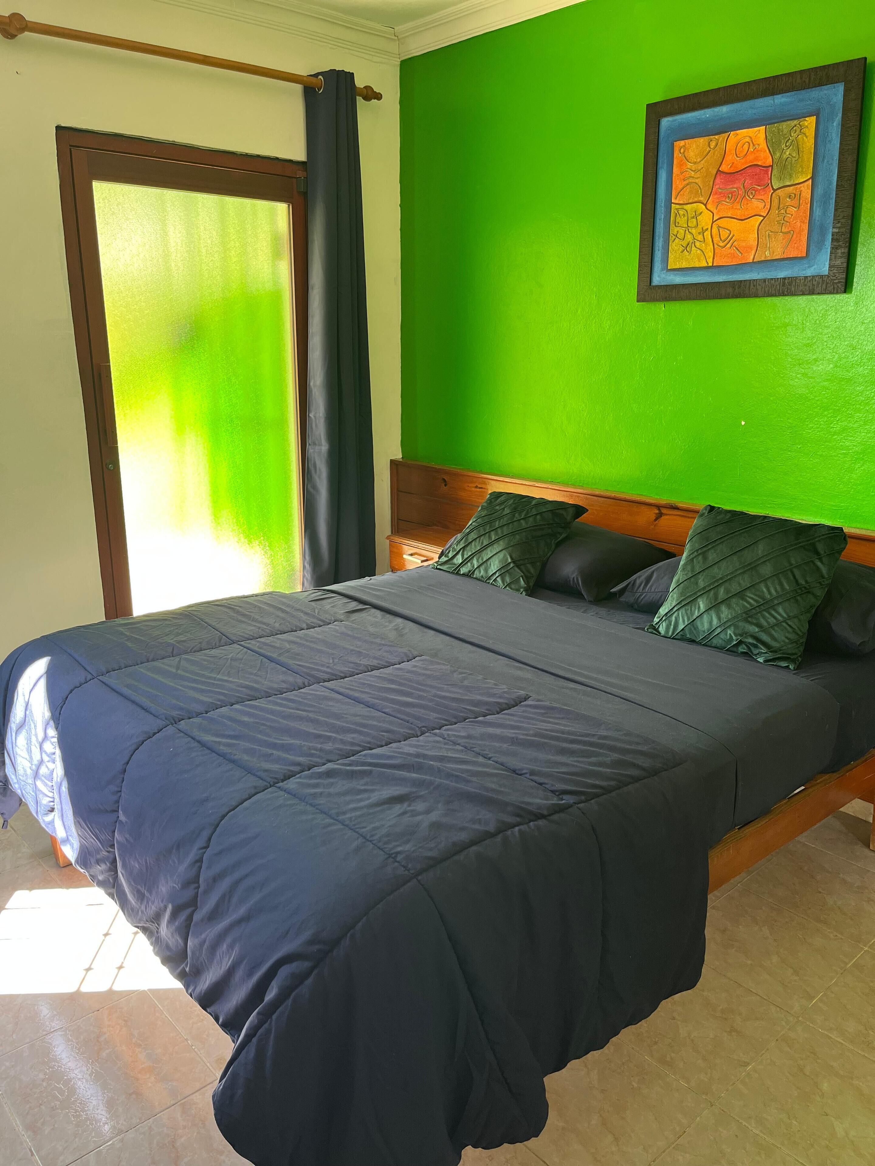 A bed with a dark blue bedspread, a wooden headboard, and two green pillows.