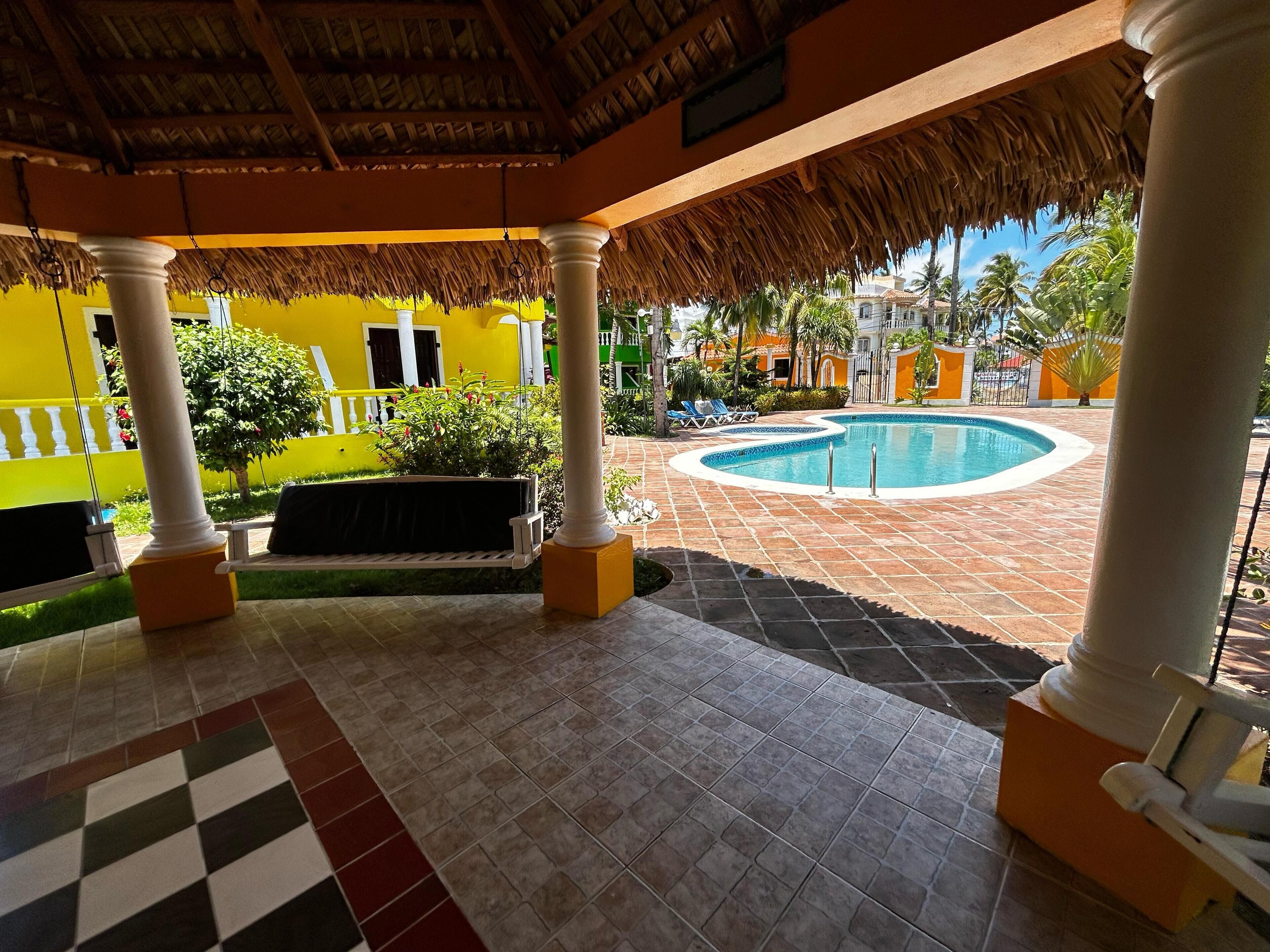 A covered outdoor area with a pool, columns, and a checkered floor.