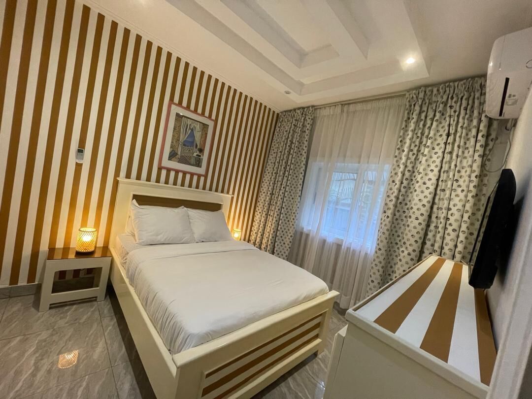 Ein Hotelzimmer mit einem Bett, einem Nachttisch, einem Fenster mit Vorhängen und einer Klimaanlage.