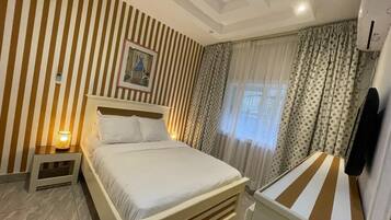 Ein Hotelzimmer mit einem Bett, einem Nachttisch, einem Fenster mit Vorhängen und einer Klimaanlage.