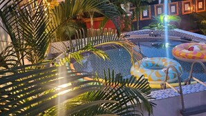Un área de piscina con una fuente, rodeada de palmeras y un solárium con baldosas.