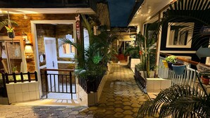 Un estrecho callejón con suelo de baldosas, plantas en macetas y una valla de madera.