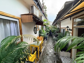 A narrow indoor corridor with tiled flooring, potted plants, and yellow chairs.