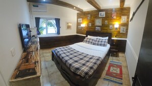 A bedroom with a large bed, a wooden dresser, a television, and a wall-mounted air conditioner.