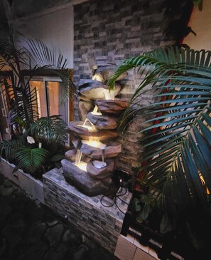 A stone waterfall feature with cascading water, surrounded by lush tropical plants.