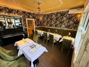 A restaurant with a piano, green upholstered chairs, and white tablecloths.