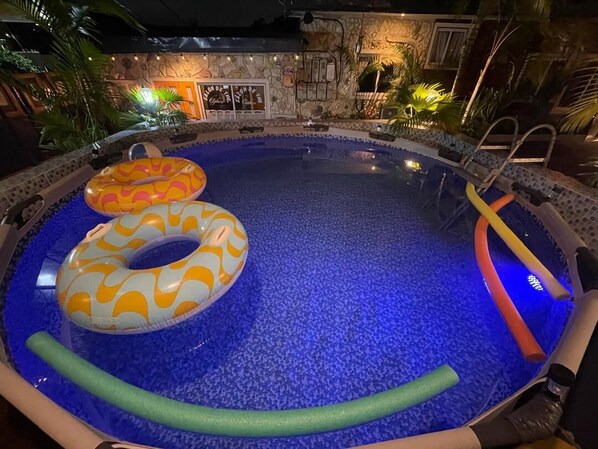 A swimming pool with blue mosaic tiles, two inflatable rings, and a ladder.