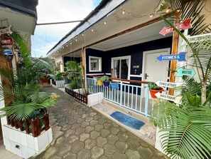 A hotel with a covered outdoor area, potted plants, and directional signs for various amenities like office, fitness, and heritage.