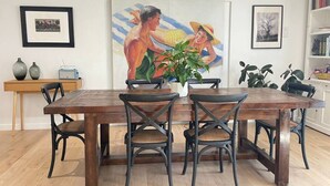 Un comedor con una mesa de madera y cuatro sillas, una planta en maceta y obras de arte en las paredes.