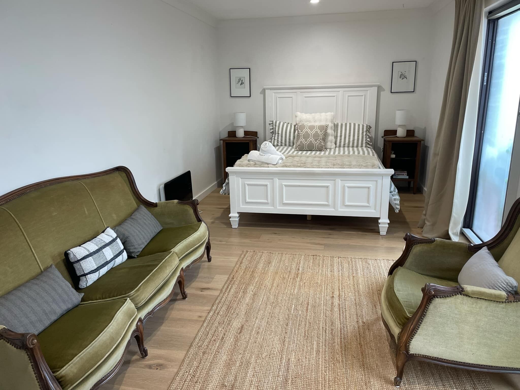 A bedroom with a large bed, two nightstands, a green sofa, and a chair.