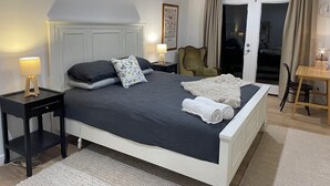Una cama bien hecha con una colcha azul oscuro, dos lámparas de noche, una silla y una mesa con lámpara.